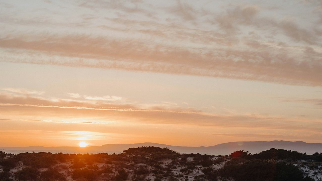 The sun setting over the dunes of Comporta, the hills of Arrábida on the horizon
