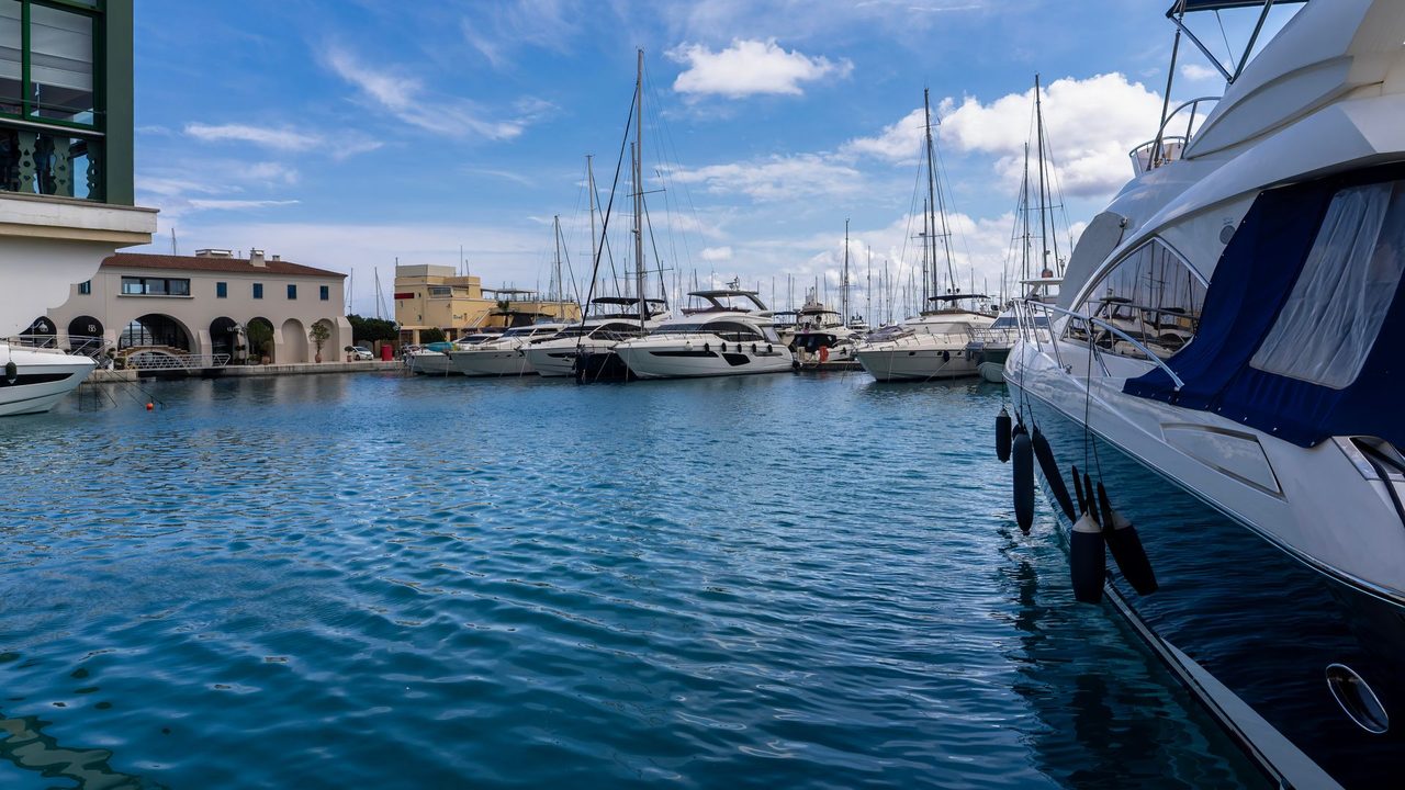 Yachts moored in Limassol Marina under a blue sky, the harbour buildings behind