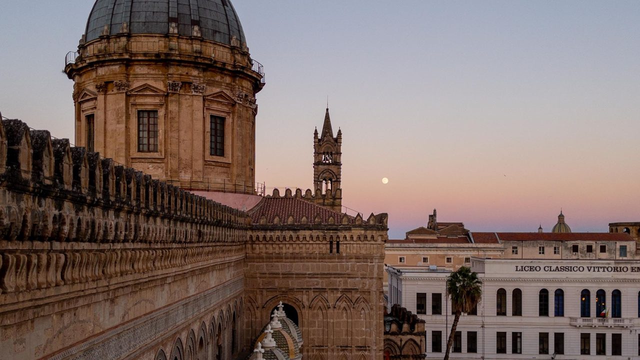 The dome and bell tower of Palermo Cathedral from its roof at dusk, the tiled cupolas below