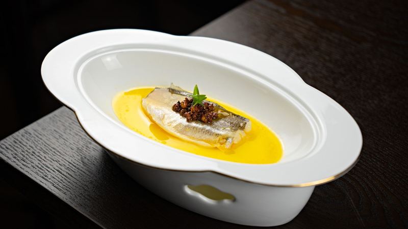 A fillet of fish in golden sauce, served in a white dish on a dark table