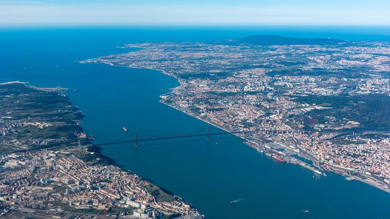 Lisbon and the 25 de Abril Bridge over the Tagus from the air, with the coast running out to Cascais and the Sintra hills beyond