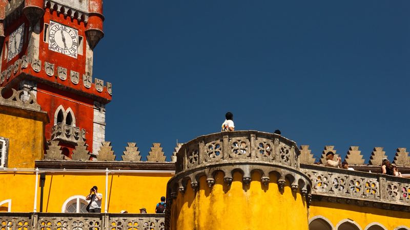 The red clock tower and yellow walls of the Pena Palace against a deep blue sky