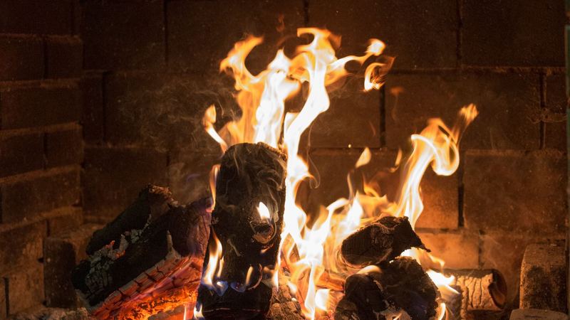 Logs blazing in an open brick fireplace, sparks rising