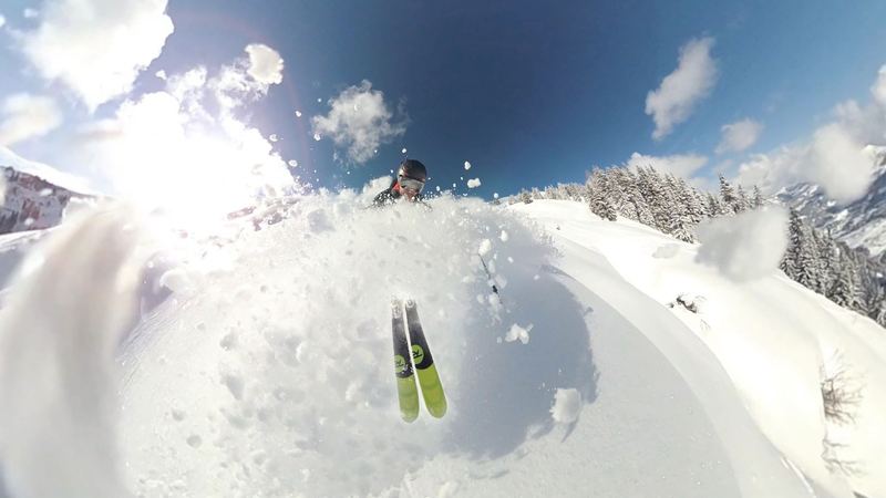 A skier bursting through deep powder below snow-laden firs on a bright day