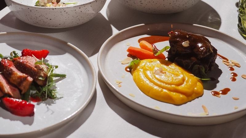 Plates of duck with strawberries and braised beef with squash purée on a white tablecloth