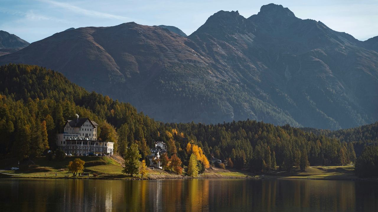 The Waldhaus am See on the shore of Lake St. Moritz in autumn, below the larch forest and the Engadine peaks