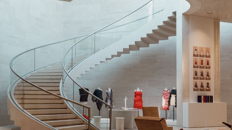 A sweeping stone staircase with glass balustrade in a boutique, dresses on display