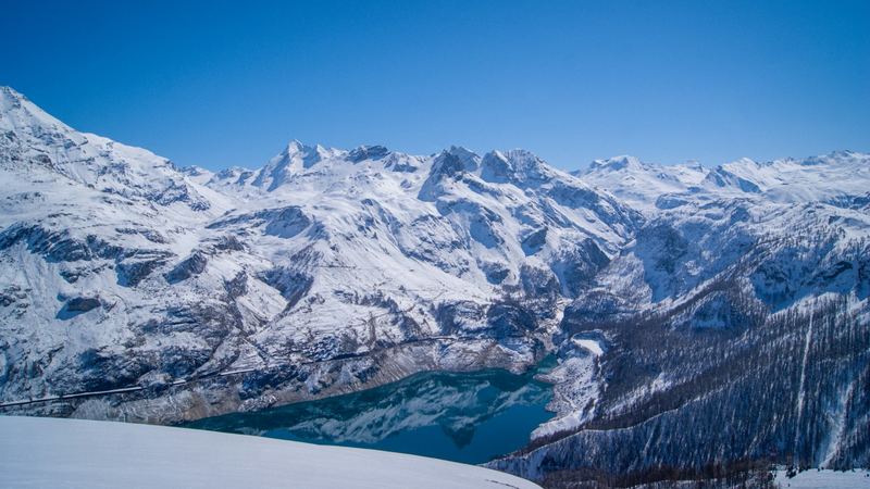 The turquoise Lac du Chevril in its snowy valley below a ring of high peaks