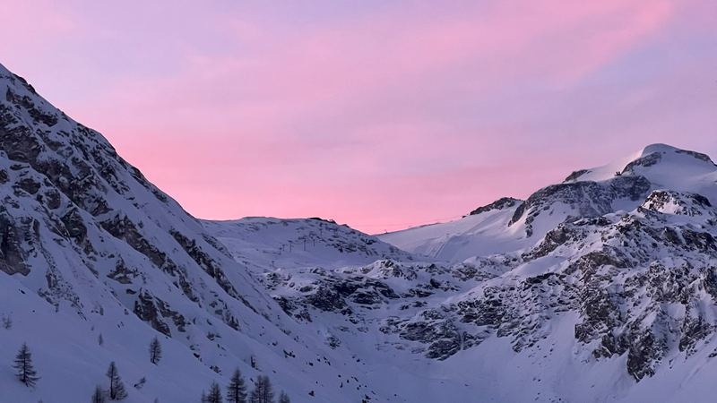 A pink and violet dusk sky over the snowy mountains and larches of the valley