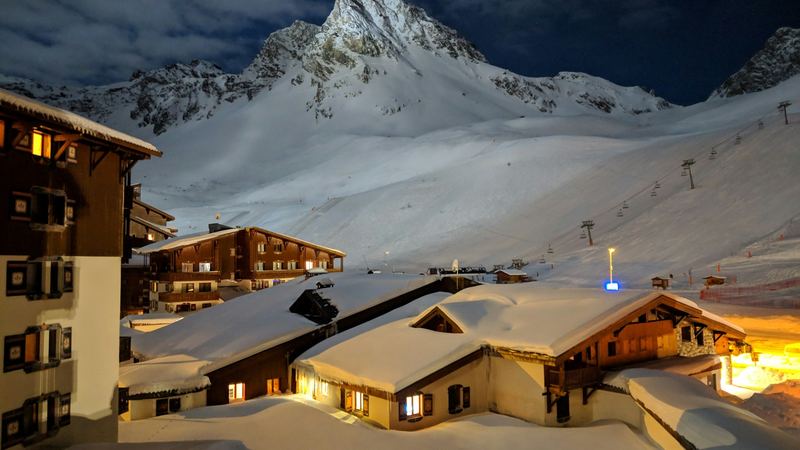 Snow-laden chalets with lit windows below a moonlit peak and the empty pistes