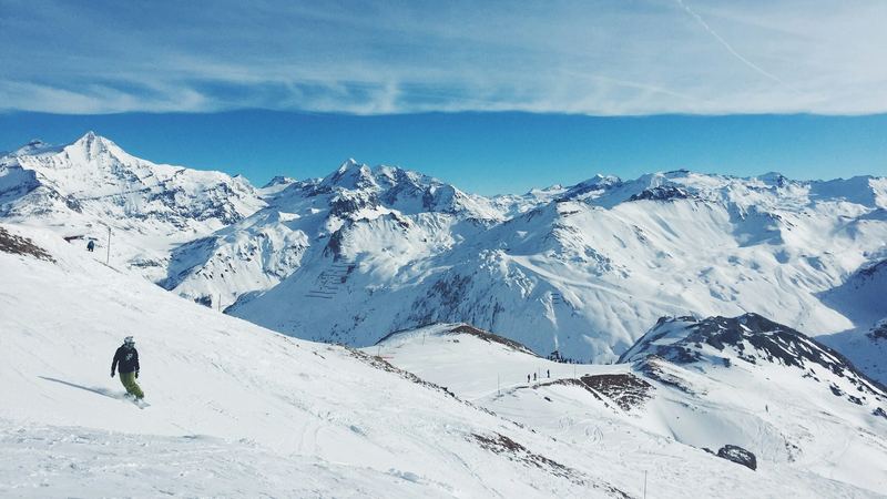 A snowboarder carving down an open slope with snowy peaks and glaciers beyond