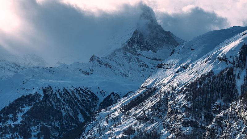 The Matterhorn in cloud above the snowy, forested slopes of the valley